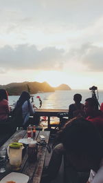 People sitting on table by sea against sky during sunset