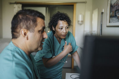 Male and female medical professionals discussing over computer in hospital