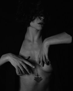 Midsection of shirtless woman with hands against black background