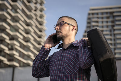 Low angle view of man talking over smart phone against buildings