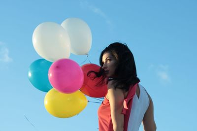 Low angle view of woman standing at balloons against sky