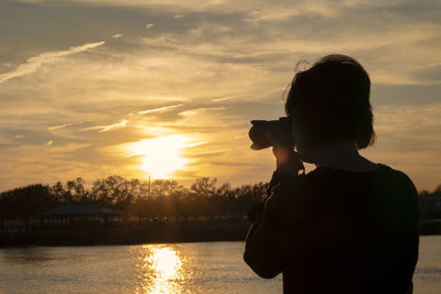 Woman photographing with camera against sky during sunset