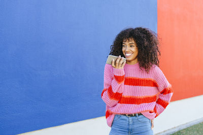 Portrait of smiling young woman sending a voice message with mobile phone