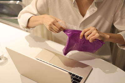 Woman is opening up packages which is wrapped in bubble wraps while sitting in front of laptop