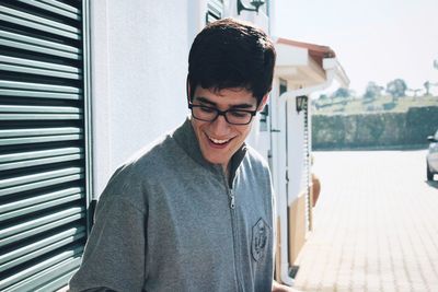 Happy young man looking down while standing against closed shutter during sunny day