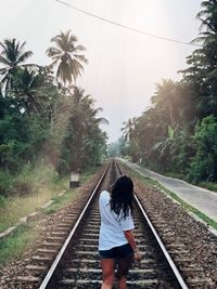 Rear view of woman walking on railroad track against sky