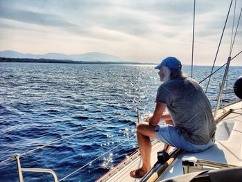 Man sitting on boat sailing in sea against sky