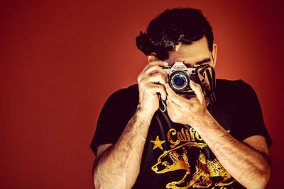 Close-up of shirtless man photographing against red background