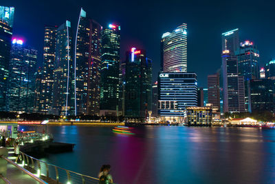 Illuminated city by river against sky at night