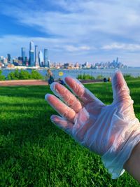 Midsection of person wearing gloves due to covid-19 restrictions raised on park against sky