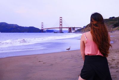 Rear view of woman standing on suspension bridge over beach