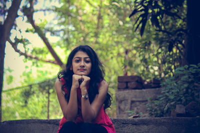 Portrait of young woman with hands on chin sitting by plants