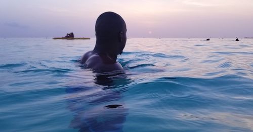 Close-up of man swimming in sea against sky during sunset