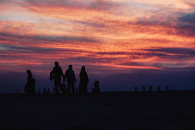 Silhouette people at beach against cloudy sky during sunset