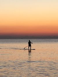 Silhouette man standing in sea against sky during sunset