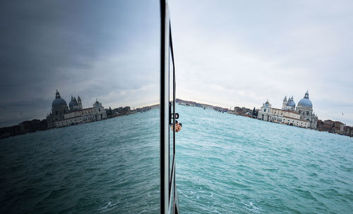 Church by sea reflecting on boat mirror against sky