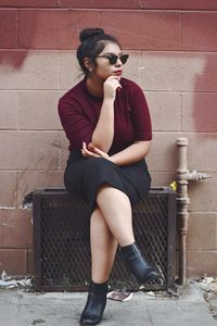Full length of young woman sitting on brick wall
