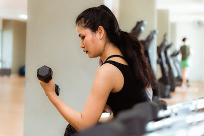 Side view of young woman exercising with dumbbell in gym