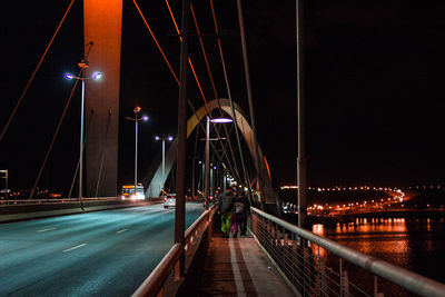 Illuminated bridge over road against sky at night