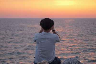 Rear view of man looking at sea during sunset