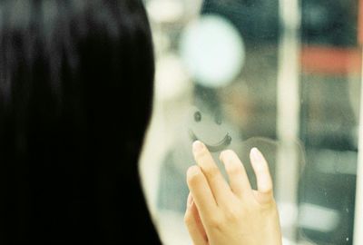 Rear view of woman making smiley face on glass window