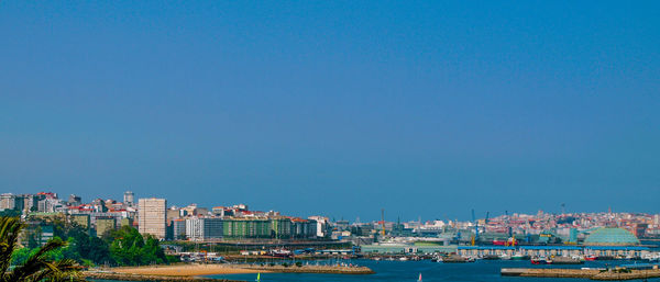 Sailboats in sea by buildings against clear blue sky