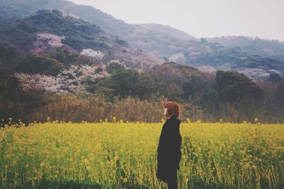 Side view of woman standing on field against mountains