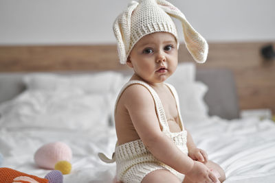 Side view of cute girl sitting on bed at home