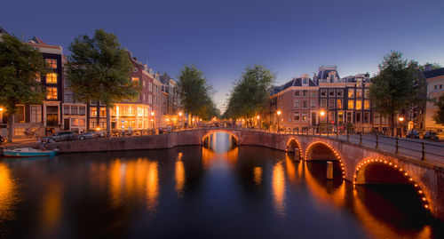 Illuminated buildings by river against sky at night