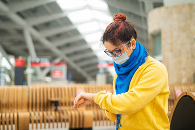 Woman wearing mask checking time outdoors