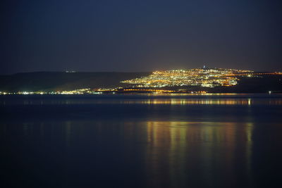 Aerial view of sea by illuminated city against sky at night