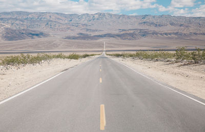 Empty road amidst field leading towards mountains