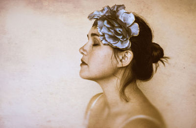 Side view of beautiful woman wearing flowers by wall