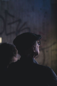 Man with hat watching into the light, a concrete wall in the background