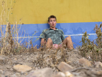 Portrait of shocked man sitting against wall