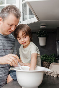 Careful dad and son toddler preparing muffin or pie dough in the kitchen. dad helps son. 