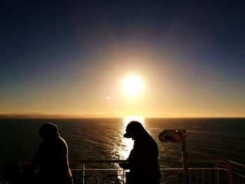 Silhouette man photographing sea against sky during sunset