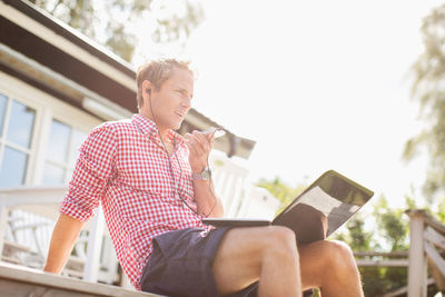 Man talking through hands-free device on porch against clear sky