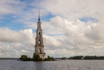 Lighthouse by building against cloudy sky