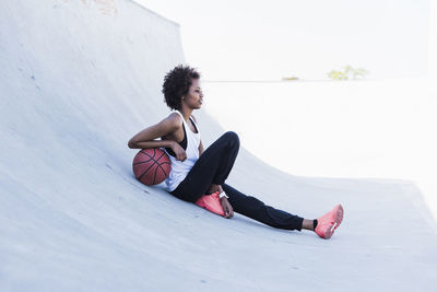 Young woman sitting with basketball outdoors