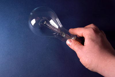 Cropped hand holding light bulb against blue background