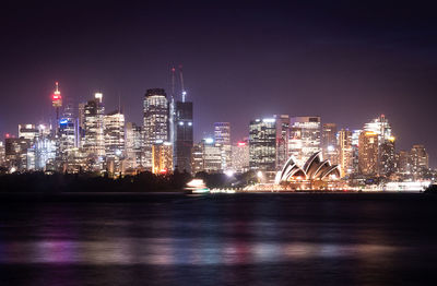 Illuminated buildings by river against sky at night