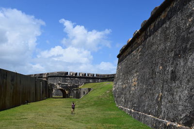 Woman standing on green field by historic building against sky