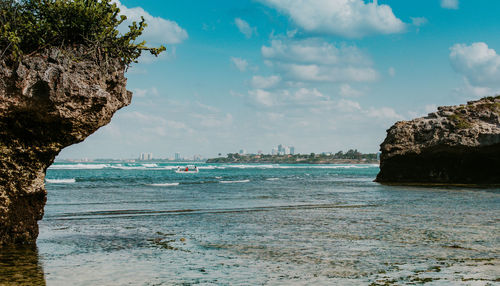 Scenic view of a boat and dar es salaam cityscape by the ocean against clouds and sky