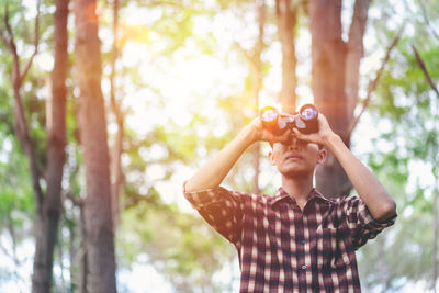 Close-up of man looking through binoculars against tree