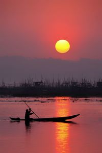 Silhouette man in boat against sky during sunset