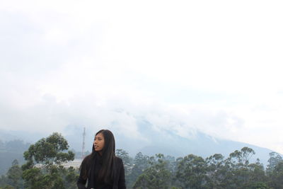 Young woman looking away while standing against sky