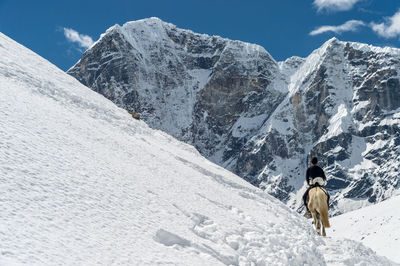 Rear view of man riding horse on snowcapped mountain against sky