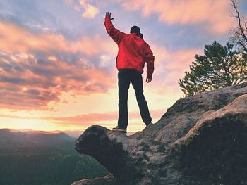 Rear view of woman standing on rock against sky during sunset