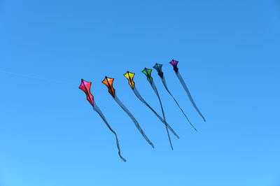 Low angle view of kites against clear blue sky